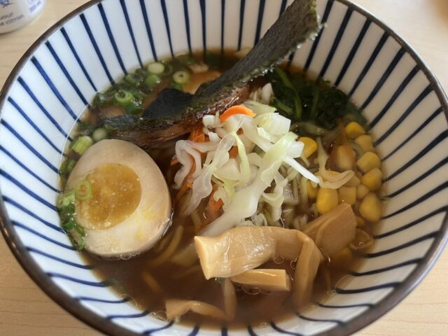 a bowl of ramen with an half a boiled egg, shredded cabbage, corn kernels, green onions, slices of bamboo shoots in soy broth