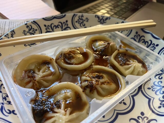 6 soup dumplings in a plastic container on a plate with chopsticks