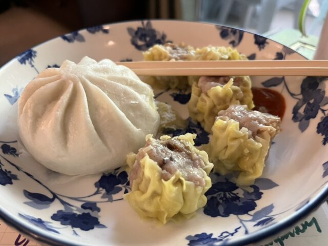 a barbeque pork bun and five pork dumplings on a plate with hot sauce and chopsticks