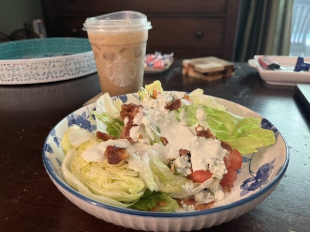 a clear plastic cup with iced coffee and a plate filled with a salad that has lettuce, bacon, tomato, and blue cheese dressing. 