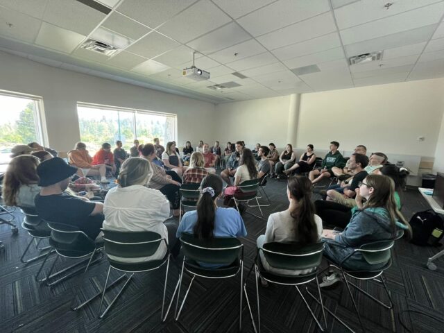 A room full of adults in a classroom sitting in chairs, formed into an inner circle and outer circle.