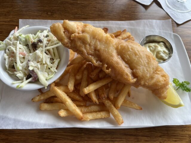 A plate of fish and chips with coleslaw, lemon wedge, and tarter sauce.