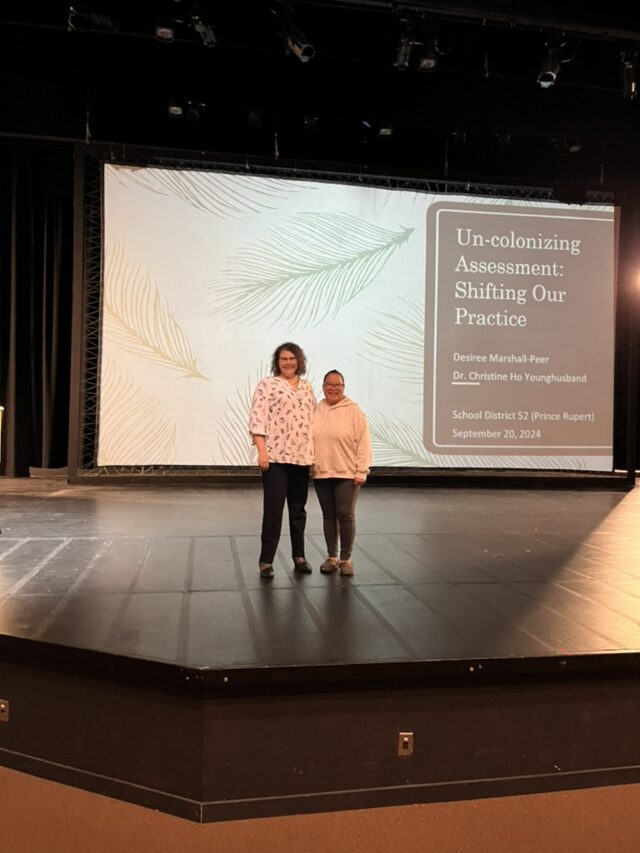 Two people standing on a stage in front of a large screen.