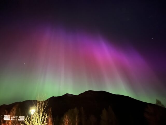 Northern Lights beaming from behind the outline of a mountain in Banff, Alberta. Photo taken in May 2024.